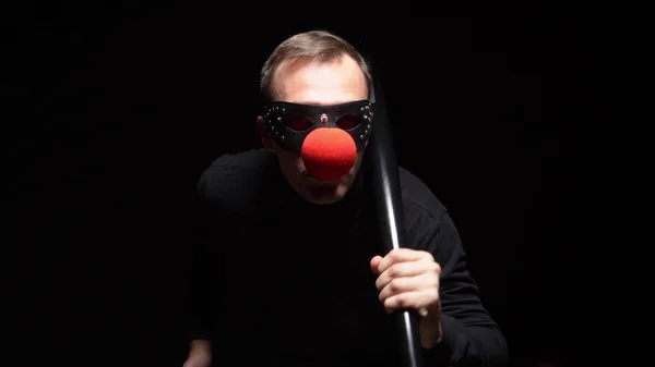 Man in een lederen masker met een rode clown neus zwaaien met een knuppel op een zwarte achtergrond — Stockfoto