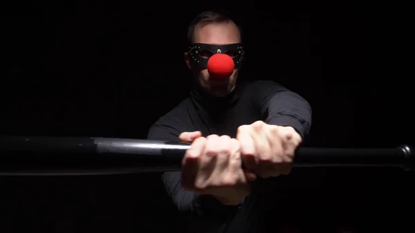 Man in een lederen masker met een rode clown neus zwaaien met een knuppel op een zwarte achtergrond — Stockfoto