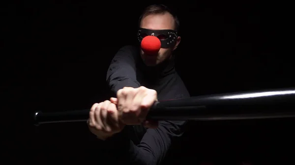 Man in een lederen masker met een rode clown neus zwaaien met een knuppel op een zwarte achtergrond — Stockfoto