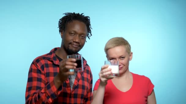 African man and Caucasian woman drink black and white cocktail. blue background — ストック動画