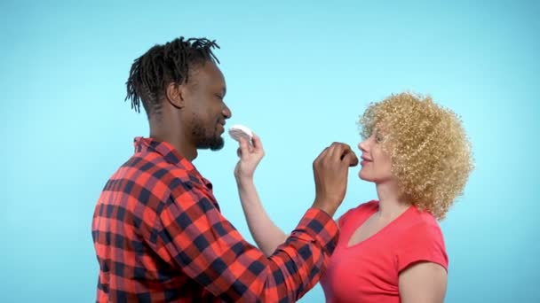 Africký muž Kavkazská žena jí černé a bílé marshmallows. modré pozadí — Stock video