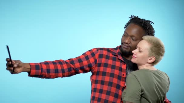 Африканский парень и белая девушка делают селфи со смартфоном. голубой фон . — стоковое видео