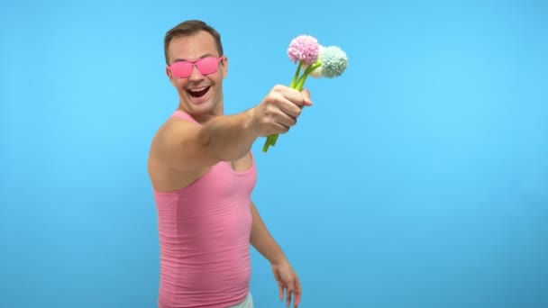 Jóképű férfi rózsaszín szemüvegben egy csokor virággal. kék háttér — Stock videók