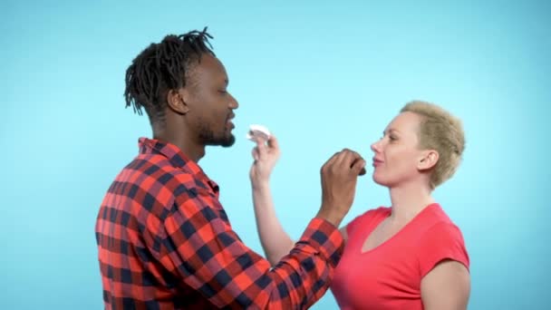 Αφρικανός άνδρας Καυκάσια γυναίκα τρώει ασπρόμαυρα ζαχαρωτά. μπλε φόντο — Αρχείο Βίντεο
