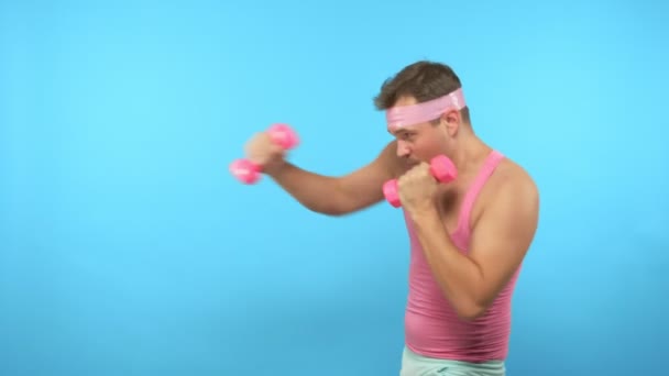 Juguetón hombre guapo en una camisa rosa se dedica a la aptitud con mancuernas de color rosa . — Vídeos de Stock