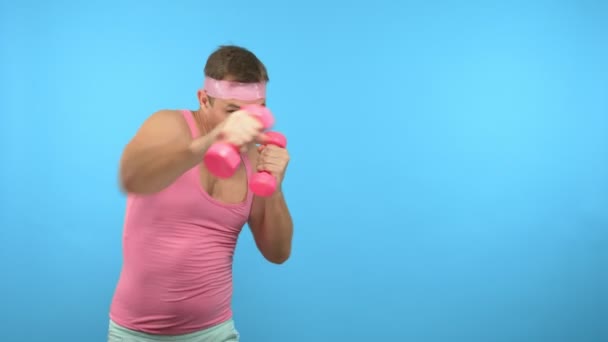 Bel homme ludique dans une chemise rose est engagé dans la forme physique avec des haltères roses . — Video