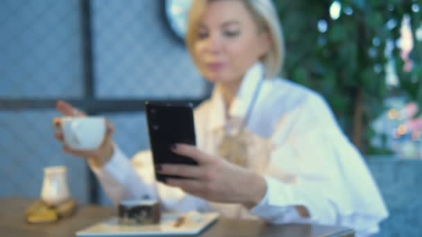 Elegante stijlvolle blonde vrouw met behulp van mobiele telefoon zitten in een cafe — Stockvideo