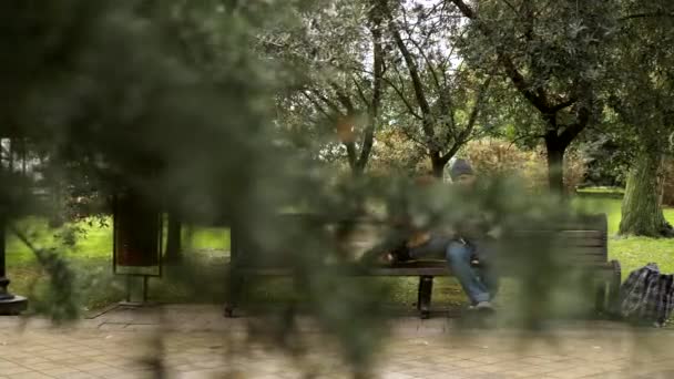 一对无家可归的夫妇，一个男人和一个女人坐在城市公园的长椅上 — 图库视频影像