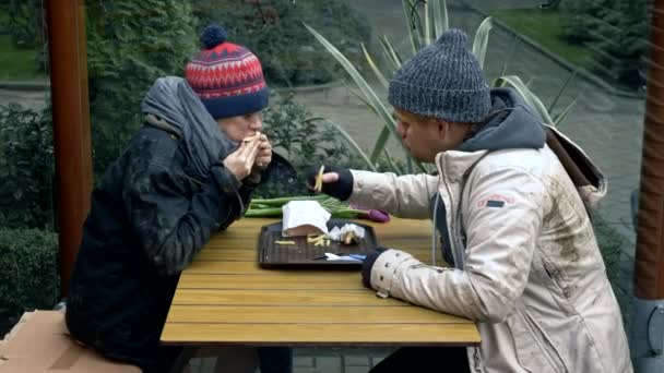 Hemlösa par, man och kvinna äter rester från ett bord på ett gatucafé — Stockvideo