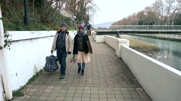 Par hemlösa man och kvinna med en hund promenad längs vallen av floden — Stockvideo