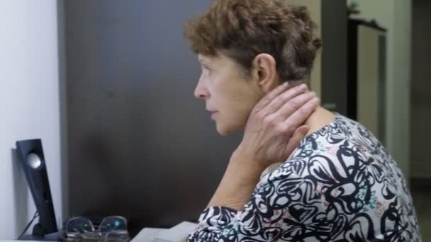 Anciana en la computadora se sienta en una mesa en la oficina del hogar — Vídeo de stock