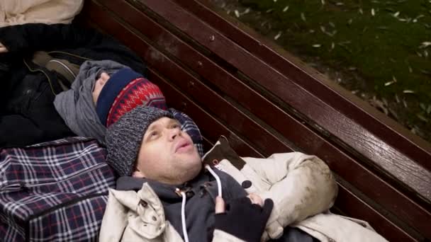 Un couple de SDF, un homme et une femme sur un banc dans un parc de la ville — Video