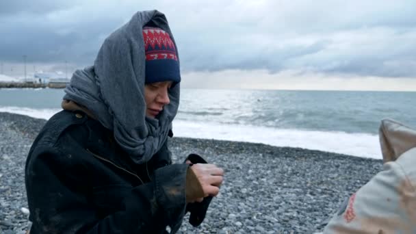 Бездомная пара, мужчина и женщина курят на берегу моря — стоковое видео