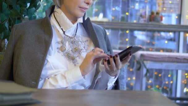 Elegante donna bionda elegante utilizzando il telefono cellulare seduto in un caffè — Video Stock