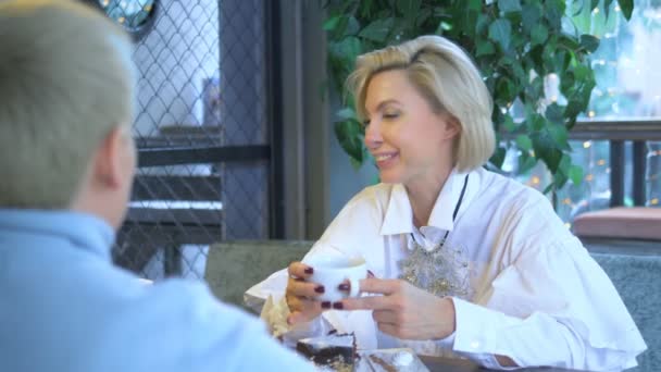 दो सुंदर स्टाइलिश महिलाओं सुनहरे बालों वाली एक कैफे में बैठे संवाद — स्टॉक वीडियो