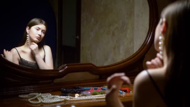 Όμορφο κορίτσι βάζει σκουλαρίκια, κάθεται μπροστά στον καθρέφτη το σούρουπο. — Αρχείο Βίντεο