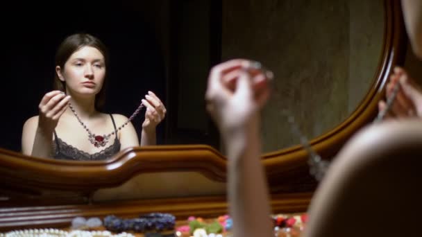 Gyönyörű lány visel nyakláncot ül a tükör előtt az alkonyatban. — Stock videók