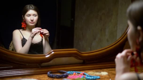 Menina bonita coloca brincos, sentado na frente do espelho ao entardecer . — Vídeo de Stock