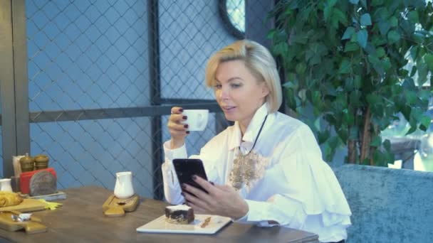 Elegante mulher loira elegante usando telefone móvel sentado em um café — Vídeo de Stock