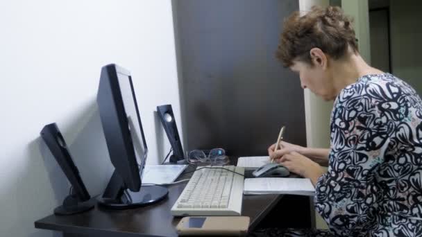 Äldre kvinna vid datorn sitter vid ett bord på hemmakontoret — Stockvideo