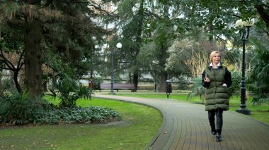 Sonbaharda bir şehir parkında yürüyen şık, şık, sarışın bir kadın.
