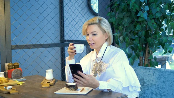 Елегантна стильна блондинка, використовуючи мобільний телефон, сидить у кафе — стокове фото