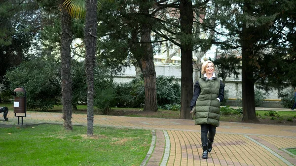 Sonbaharda bir şehir parkında yürüyen şık, şık, sarışın bir kadın.