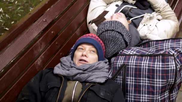 Un couple de SDF, un homme et une femme sur un banc dans un parc de la ville — Video