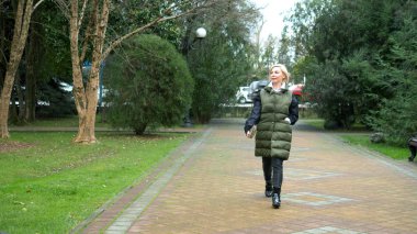 Sonbaharda bir şehir parkında yürüyen şık, şık, sarışın bir kadın.