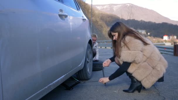 Két lány kereket cserél a kocsin az út szélén.. — Stock videók