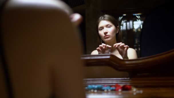 Красива дівчина одягає сережки, сидячи перед дзеркалом в сутінках . — стокове відео