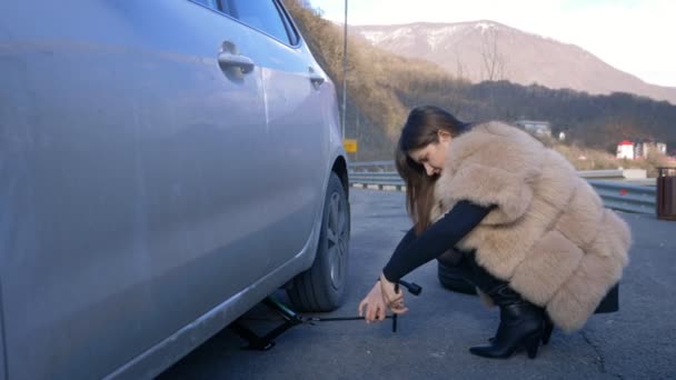 Bella ragazza che cambia la ruota di una macchina parcheggiata sul ciglio della strada — Video Stock