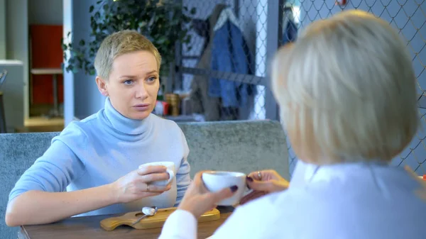 Dos hermosas mujeres con estilo rubias se comunican sentado en un café — Foto de Stock