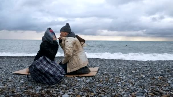 Hemlösa par, man och kvinna röker på stranden — Stockvideo