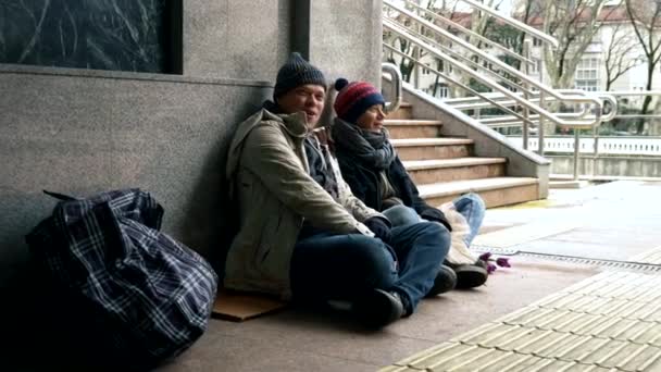 Hemlösa ber om allmosor sittande på trottoaren mot väggen — Stockvideo