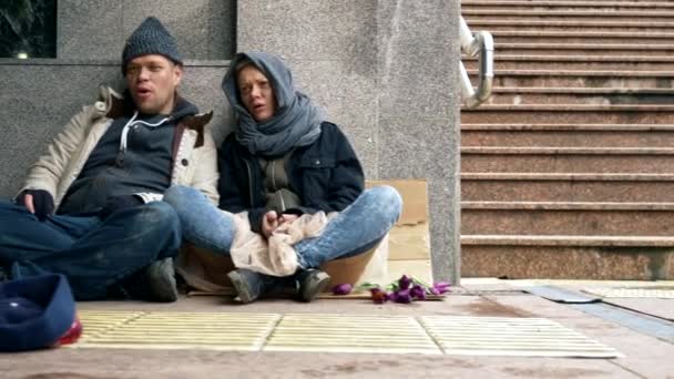 Vagabundos piden limosna sentados en la acera contra la pared — Vídeos de Stock