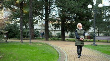 Sonbaharda bir şehir parkında yürüyen şık, şık, sarışın bir kadın.