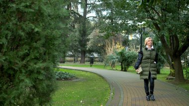 Sonbaharda bir şehir parkında yürüyen şık, şık, sarışın bir kadın.