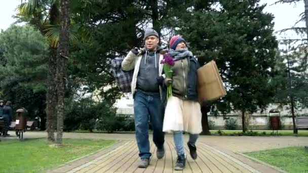 Een paar dakloze mannen en een vrouw lopen in een stadspark — Stockvideo