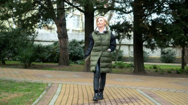 Sonbaharda bir şehir parkında yürüyen şık, şık, sarışın bir kadın.