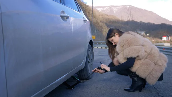 Beautiful girl changing the wheel of a car parked on the roadside — Stock Photo, Image