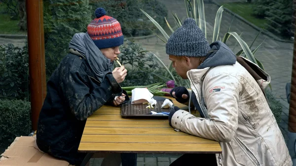 Pareja sin hogar, hombre y mujer comiendo sobras de una mesa en un café de la calle — Foto de Stock