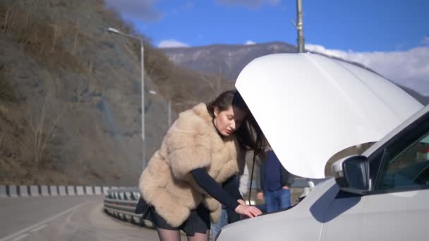 Flickan tittar under stötfångaren på bilen, män tar bort den på telefonen — Stockvideo