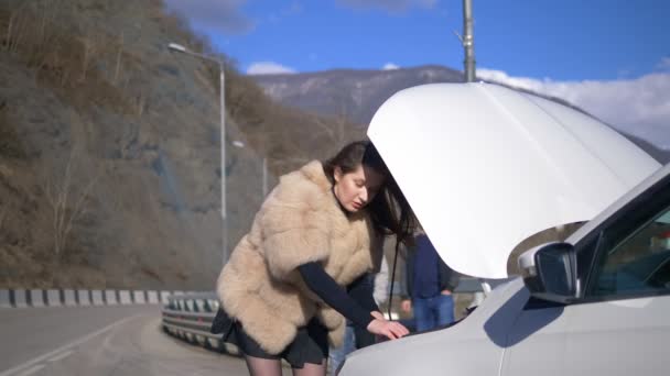 La chica mira debajo del parachoques del coche, los hombres lo quitan por teléfono — Vídeos de Stock