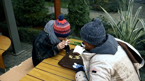 Pasangan tunawisma, pria dan wanita makan sisa makanan dari meja di kafe jalanan — Stok Foto