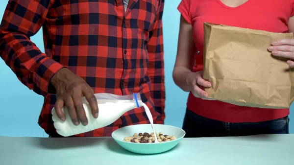 Африканский мужчина, белая женщина, делает хлопья на завтрак с молоком. голубой фон — стоковое фото