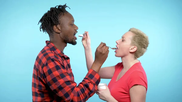 Afrikaanse man Blanke vrouw die chocolade en romige yoghurt eet. blauwe achtergrond — Stockfoto