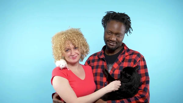 Hombre africano y mujer caucásica. sosteniendo un gato negro y una rata blanca . — Foto de Stock