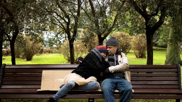 Para bezdomnych, mężczyzna i kobieta na ławce w parku miejskim — Zdjęcie stockowe