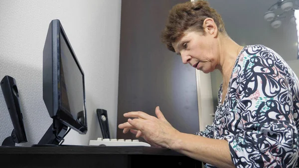 Idős nő a számítógépnél ül egy asztalnál az otthoni irodában — Stock Fotó